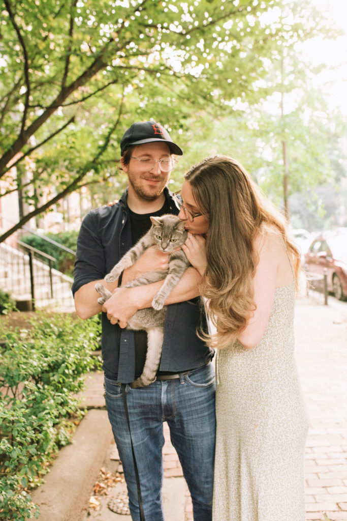 man smiles at woman as she embraces the cat in his arms and gives the cat a kiss