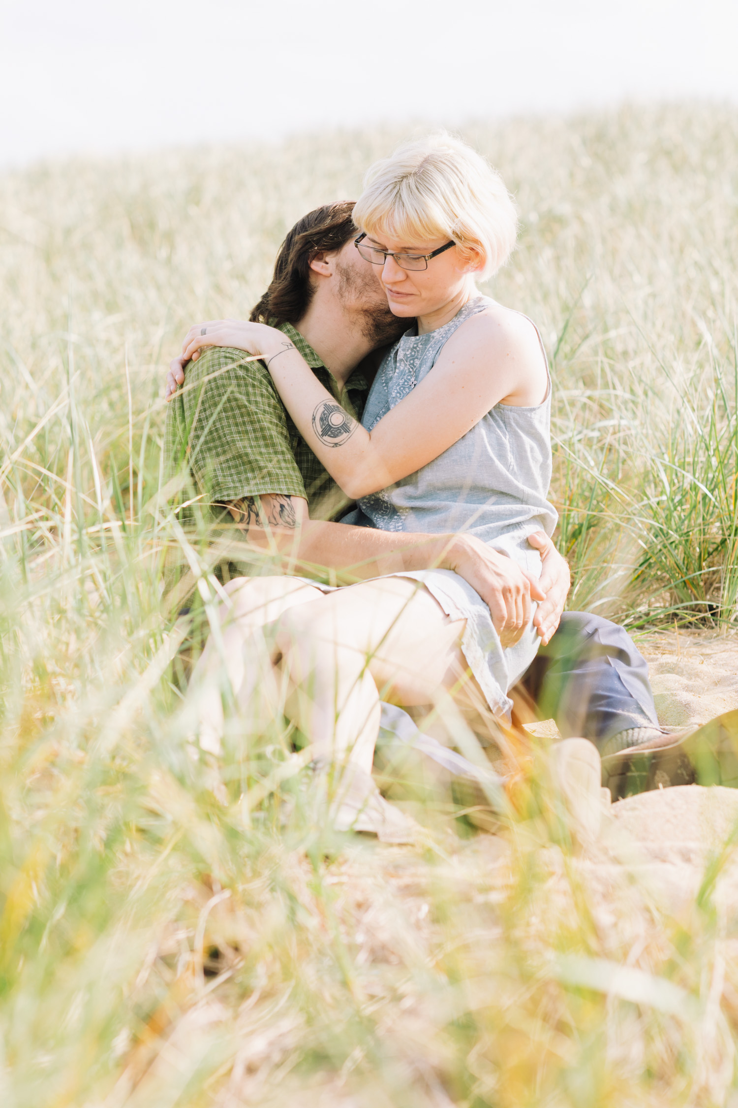 Woman sits on mans lap in a field of beach grass